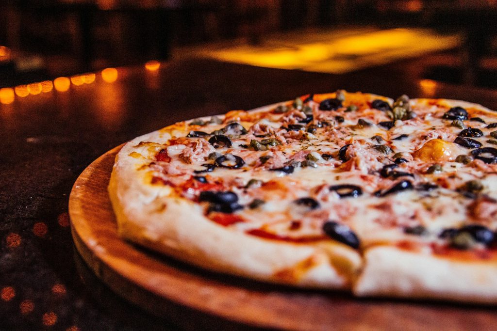 Close-up of a vegetable pizza with olives on a wooden board in a cozy restaurant setting.