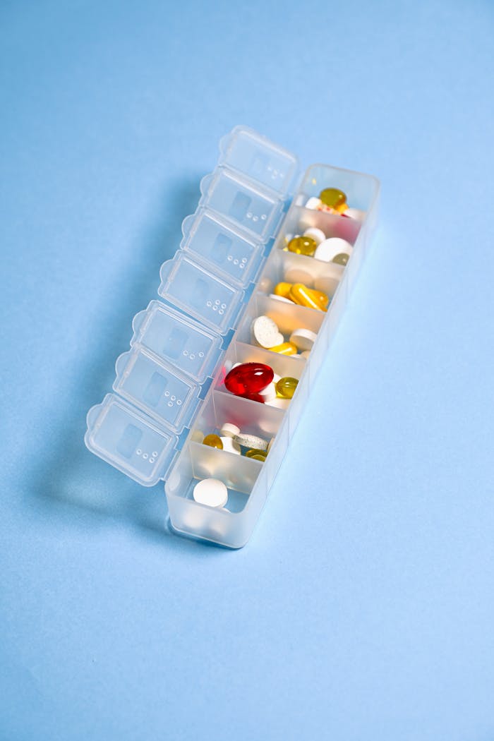 Colorful pills and capsules organized in a weekly pill container against a blue background.